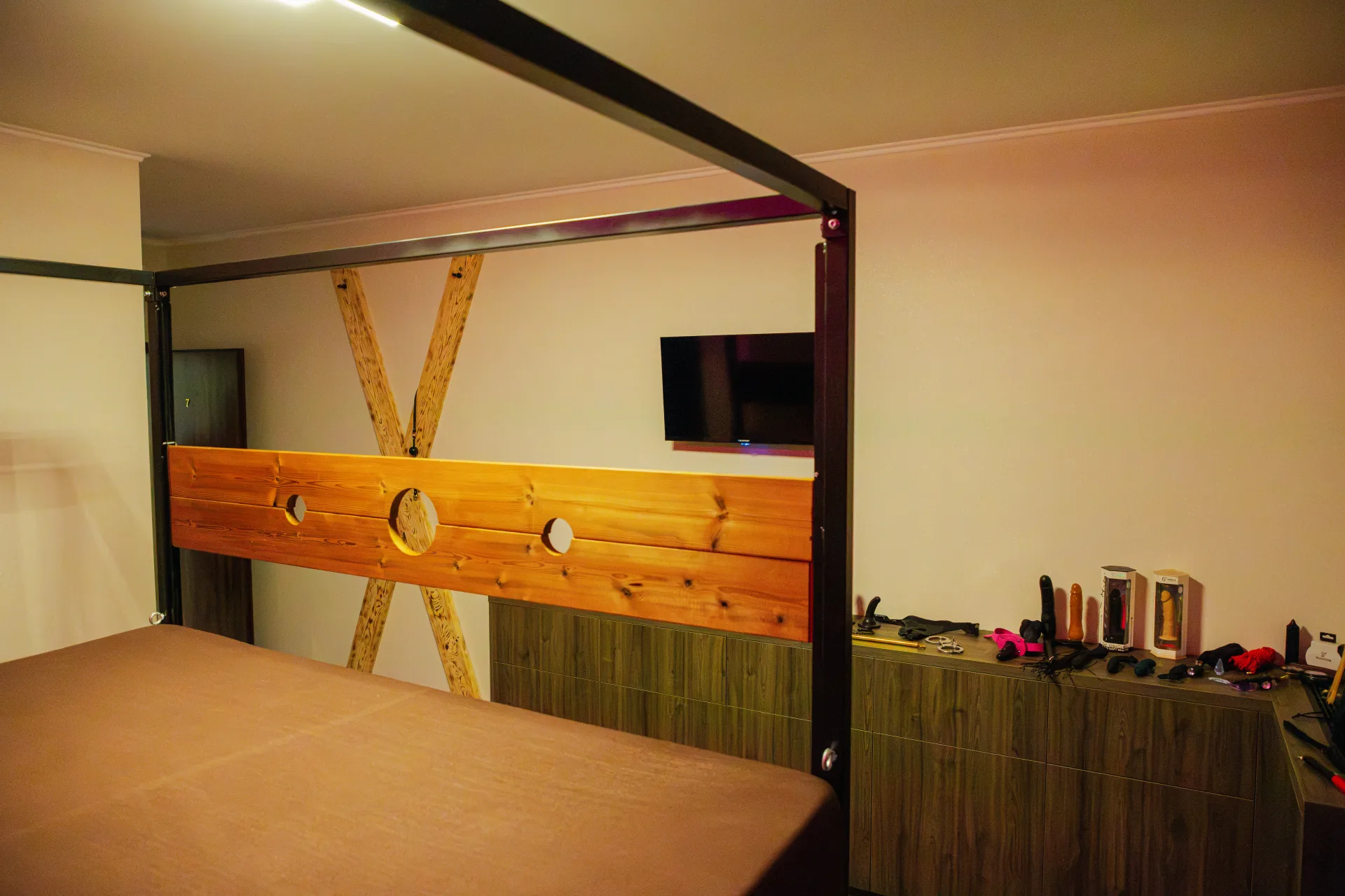 Blick durch die Metallkonstruktion auf das hölzerne Andreaskreuz an der Wand, den Fernseher und die Kommode mit Accessoires