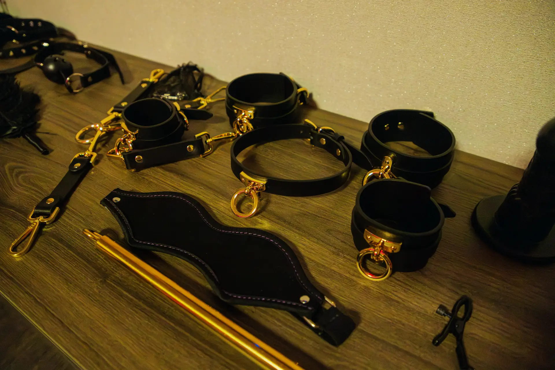 Detail der Accessoires auf der Kommode: schwarze Lederfesseln und Halsband mit goldenen Beschlägen